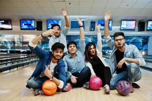 groep van vijf Zuid-Aziatische volkeren die rust en plezier hebben in de bowlingclub, zittend op een bowlingbaan met ballen op handen. foto