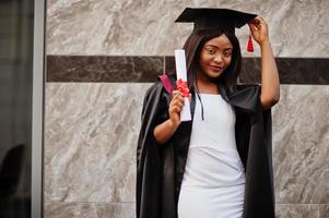 jonge vrouwelijke Afro-Amerikaanse student met diploma poseert buitenshuis. foto