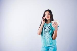 portret van een aantrekkelijk meisje in blauw of turquoise t-shirt en broek poseren met veel geld en smartphone in haar handen. foto