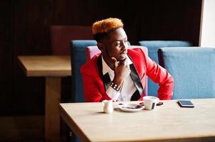 mode Afro-Amerikaanse man model in rood pak, met hoogtepunten haar zittend in café met koffie. foto