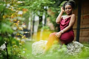 portret van een mooie natuurlijke jonge afrikaanse vrouw met afrohaar. zwart model in rode zijden jurk. foto