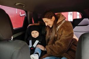 jonge moeder en kind in auto. kinderzitje op stoel. veiligheid rijden concept. foto