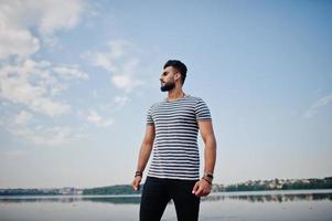 knappe lange arabische baard man model op gestript shirt poseerde buiten tegen het meer en de lucht. modieuze Arabische man. foto