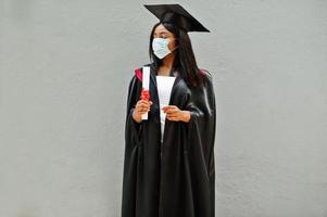 jonge vrouwelijke afro-amerikaanse afgestudeerde student draagt een beschermend masker tegen coronavirus. concept van diploma-uitreiking, quarantaine. foto