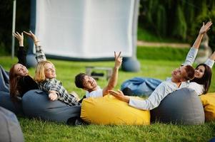 jonge multi-etnische groep mensen kijken naar film op poef in openluchtbioscoop. foto