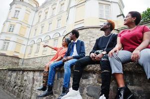 vier Afrikaanse vrienden die buiten plezier hebben. twee zwarte meisjes met jongens zitten in een oude stad. foto