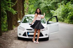 Afro-Amerikaanse vrouw poseerde tegen witte auto in bosweg. foto