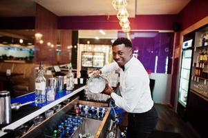 Afro-Amerikaanse barman bij bar met ijsemmer. bereiding van alcoholische dranken. foto