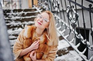 portret van blond meisje in glazen, rode bontjas en sjaal op winterdag. foto