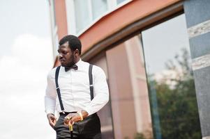 knappe modieuze Afro-Amerikaanse man in formele kleding, vlinderdas en bretels, wandelstok. foto