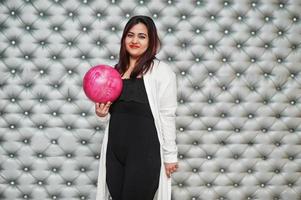 stijlvolle Aziatische vrouw met roze bowlingbal bij de hand tegen zilveren muur achtergrond. foto