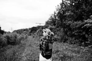 portret van een aantrekkelijk blond meisje in tartan shirt met rugzak wandelen op het platteland. foto