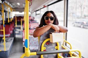 jonge stijlvolle Afro-Amerikaanse vrouw in moderne zonnebril rijden op een bus. foto