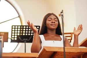 Afro-Amerikaanse vrouw bidden in de kerk. gelovigen mediteren in de kathedraal en geestelijke gebedstijd. afro meisje zingt en verheerlijkt god op refreinen. foto