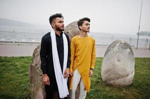 twee Indiase stijlvolle mans vrienden in traditionele kleding poseerden buiten tegen grote stenen. foto
