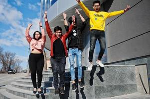 groep aziatische mensen vrienden staan op trappen buiten tegen modern gebouw en springen samen. foto