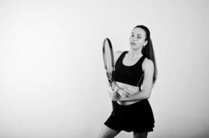 zwart-wit portret van een mooie jonge vrouw in sportkleding die een tennisracket vasthoudt terwijl hij tegen een witte achtergrond staat. foto