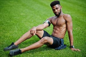 Afro-Amerikaanse mannelijke atleet sexy sport blote torso man met lopende sport arm case voor mobiele telefoon, gesteld op groen gras van voetbalstadion. foto