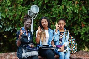 drie afrikaanse studenten vrouw poseerde met rugzakken en schoolspullen op het erf van de universiteit en toont een goed teken met de handen. foto