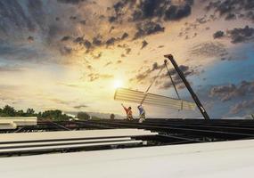 arbeiders installeren nieuwe daken met behulp van mobiele kranen. til de metalen dakplaat op het plafondframe op. ga naar boven om boven het stalen framedak op het bouwproject op te slaan. foto