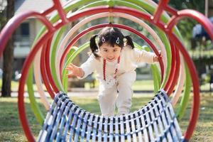 schattig aziatisch meisjesspel op school of kleuterschool of speelplaats. gezonde zomeractiviteit voor kinderen. klein Aziatisch meisje buiten klimmen op speelplaats. kind spelen op buitenspeeltuin. foto