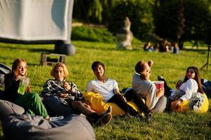 jonge multi-etnische groep mensen kijken naar film op poef in openluchtbioscoop. foto