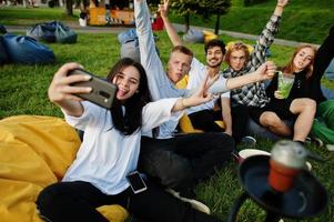 jonge multi-etnische groep mensen kijken naar film op poef in openluchtbioscoop en maken selfie op telefoon. foto