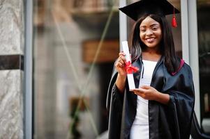 jonge vrouwelijke Afro-Amerikaanse student met diploma poseert buitenshuis.