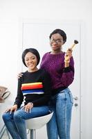 Afro-Amerikaanse vrouw die make-up toepast door visagist bij beauty salon. foto