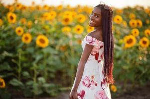 mooie jonge zwarte vrouw draagt zomerjurk pose in een zonnebloemveld. foto