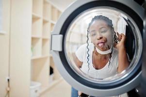 grappig portret van vrolijke Afro-Amerikaanse vrouw in de buurt van wasmachine in de zelfbedieningswasserette. foto