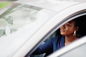 rijke zakelijke afrikaanse vrouw zit op de bestuurdersstoel bij zilveren suv-auto met geopende deur. foto