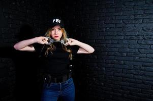 FBI vrouwelijke agent in pet en met pistool in studio tegen donkere bakstenen muur. foto