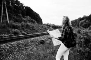 portret van een mooi blond meisje in tartan shirt wandelen op de spoorlijn met kaart in haar handen. foto
