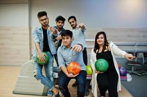 groep van vijf Zuid-Aziatische volkeren die rust en plezier hebben bij de bowlingclub. bowlingballen bij de hand houden en vingers aan de camera laten zien. foto