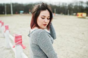 portret van brunette meisje in grijze jurk zit op witte houten constructie. foto