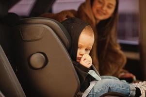 jonge moeder en kind in auto. kinderzitje op stoel. veiligheid rijden concept. foto