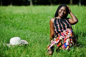 portret van prachtige Afro-Amerikaanse vrouw 20s in zomerhoed zittend op groen gras in het park. foto