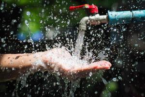 waterconcept in het dagelijks leven. handen ondersteunen het water dat uit de kraan stroomt. water dat uit de kraan spat foto