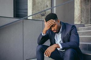 Afrikaanse zakenman zit gefrustreerd op de trap, depressief door de resultaten van zijn werk foto