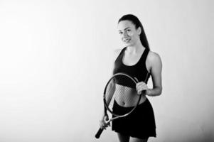 zwart-wit portret van een mooie jonge vrouw in sportkleding die een tennisracket vasthoudt terwijl hij tegen een witte achtergrond staat. foto