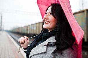 brunette meisje in grijze jas met rode paraplu in treinstation. foto