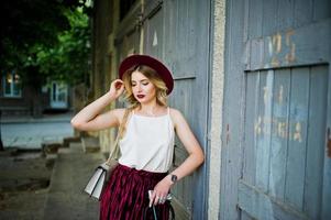 modieuze en mooie blonde model meisje in stijlvolle rood fluwelen velours rok, witte blouse en hoed, gesteld met telefoon en koptelefoon. foto