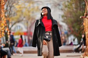 afro-amerikaanse mode meisje in jas en krantenverkoper pet, met handtas gesteld op straat. foto