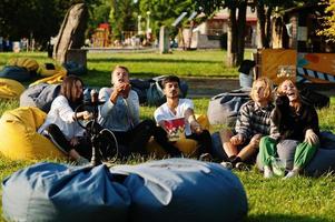 jonge multi-etnische groep mensen die film kijken op poef en popcorn in openluchtbioscoop gooien. foto