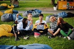 jonge multi-etnische groep mensen kijken naar film op poef in openluchtbioscoop en maken selfie op telefoon. foto