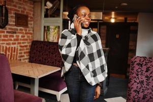 afrikaanse vrouw in geruite cape poseerde in café en sprak via de mobiele telefoon. foto