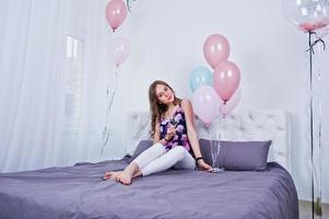 gelukkig meisje met gekleurde ballonnen op bed op kamer. verjaardag thema vieren. foto