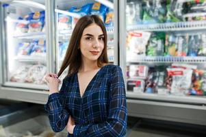 winkelende vrouw die naar de schappen in de supermarkt kijkt. portret van een jong meisje in een marktwinkel die zeevruchten uit de koelkast haalt. foto