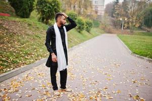 Indiase stijlvolle man in zwarte traditionele kleding met witte sjaal buiten geposeerd tegen gele herfst. foto